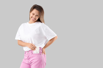 Young woman putting menstrual pad into pocket on light background