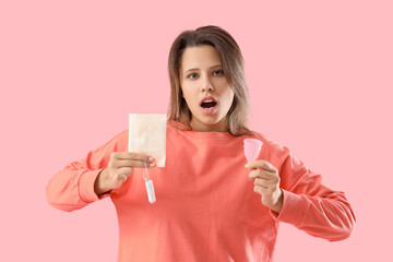 Shocked young woman with feminine hygiene products on pink background