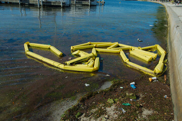 Yellow Oil Spill Containment Booms at Polluted Waterfront Scene by seawall. Booms around polluted...