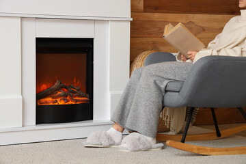 Woman in slippers and with book sitting near fireplace at home