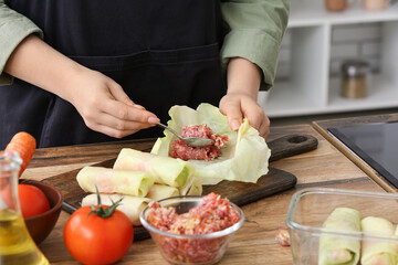 Woman preparing stuffed cabbage roll at table in kitchen, closeup