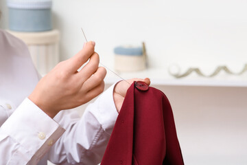 Woman sewing button on red coat in atelier, closeup