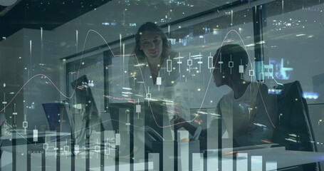 Professionals in blazers reviewing financial charts on computer in office at night, with coffee mug