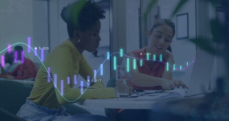 Two female coworkers pointing at charts while typing on laptops in office lounge, financial overlay