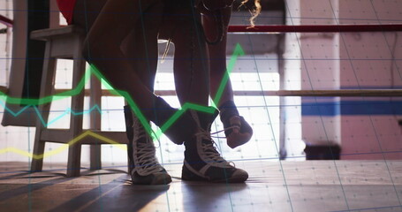 Tying high-top boxing shoe laces, boxer in athletic shorts crouching on ring platform, with graphs