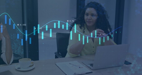 Woman in yellow blouse analyzing financial charts in meeting room, with laptop notebook coffee cup