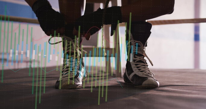 Lacing boxer kneeling and threading boot shoelaces inside boxing ring, with hand wraps, ropes