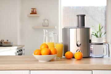 Modern juicer with oranges on table in kitchen