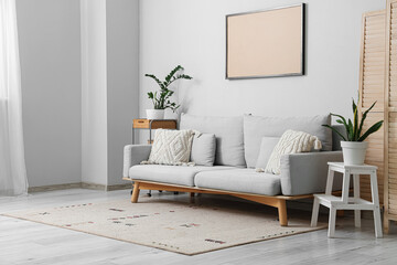 Sofa with coffee tables, houseplants and photo frame near grey wall in living room
