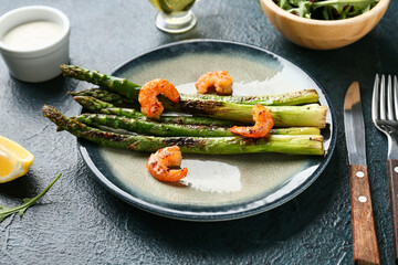 Plate with fried green asparagus and tasty shrimps on dark background, closeup