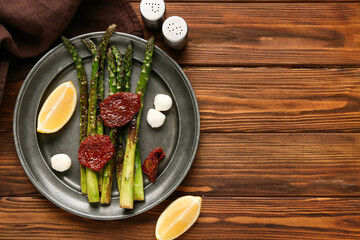 Plate of fried green asparagus with mozzarella cheese, lemon and dried tomatoes on wooden background