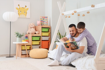Happy father with his son in pajamas reading book on bed at home