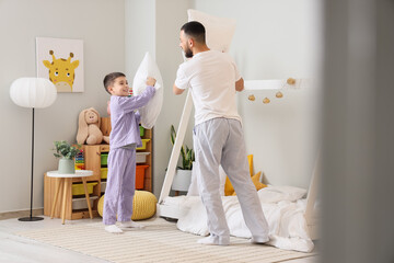 Happy father in pajamas fighting pillows with his son at home
