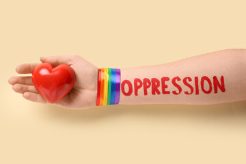 Hand with written word OPPRESSION, LGBT ribbon and red heart on beige background