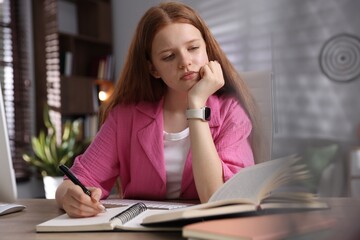 Teenage student taking notes while studying at table indoors