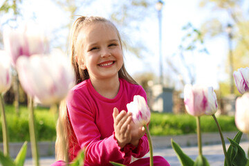 Cute little girl near beautiful pink tulips outdoors