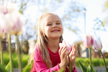 Cute little girl near beautiful pink tulips outdoors