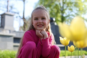 Cute little girl near beautiful yellow tulips outdoors