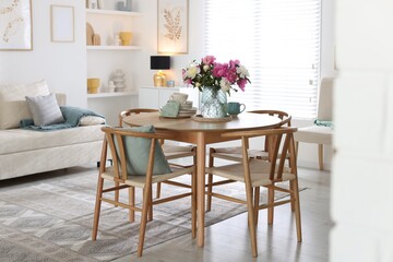Dining table with beautiful flowers and dishware in room. Interior design
