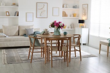 Dining table with beautiful flowers and dishware in room. Interior design