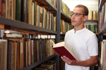 Man with book near shelves in public library