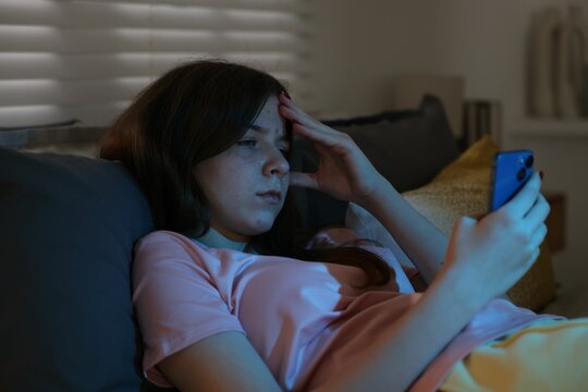 Upset teenage girl with smartphone on bed at night - Powered by Adobe