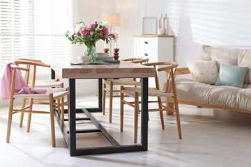 Dining table with beautiful flowers and dishware in room. Interior design