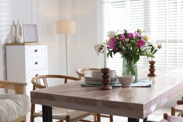 Dining table with beautiful flowers and dishware in room. Interior design