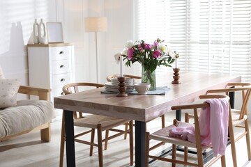 Dining table with beautiful flowers and dishware in room. Interior design