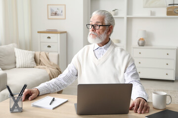Senior man learning online using laptop at desk indoors. Self-study
