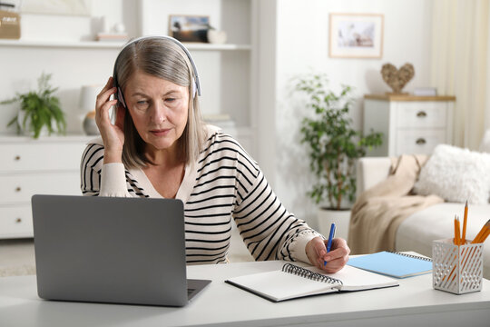 Woman learning online using laptop and taking notes at table indoors. Self-study