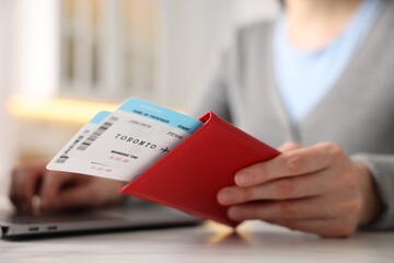 Woman with passport and flight tickets using laptop at table indoors, closeup