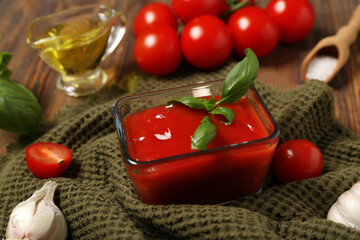 Glass bowl of tasty ketchup and different ingredients on wooden background, closeup