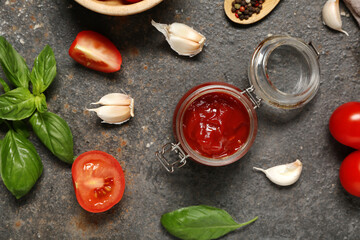 Jar of tasty ketchup and different ingredients on dark background
