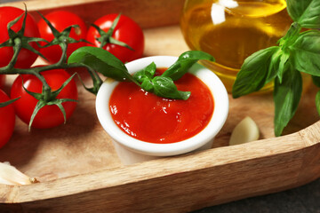 Bowl of tasty ketchup and wooden tray with different ingredients on dark background, closeup