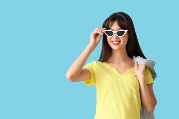 Smiling young woman in stylish sunglasses on blue background