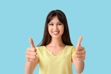 Smiling young woman showing thumbs-up on blue background