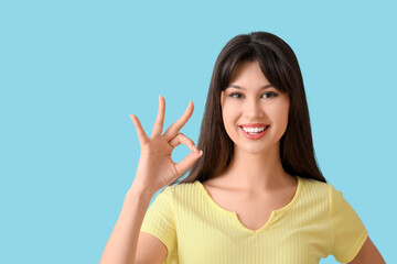 Smiling young woman showing OK on blue background
