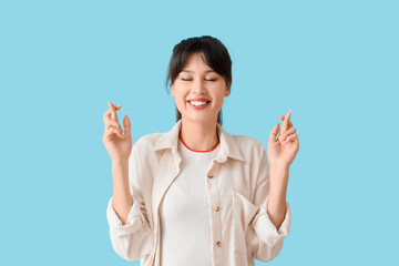 Smiling young woman crossing fingers on blue background