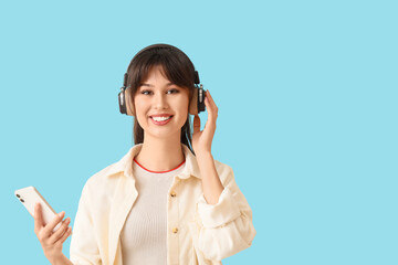 Smiling young woman in headphones with mobile phone on blue background