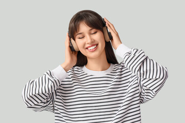 Smiling young woman in headphones on light background
