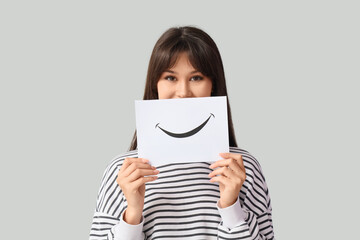 Young woman with paper smile on light background