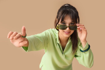 Stylish young woman in green sunglasses on beige background