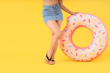 Young woman with doughnut shaped swim ring on yellow background