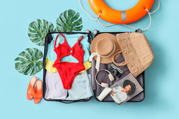 Open suitcase with beach accessories, ring buoy and palm leaves on blue background