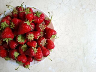 Ripe strawberries in a white plate on a marble surface