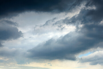Soft blue light sliver breaks through a dramatic, moody sky painted with dark storm clouds lingering overhead, showcasing hints of tranquility amidst potential turbulent weather.