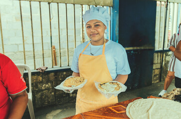 Portrait of a vendor serving and holding two pupusas. Smiling female vendor holding two plates of traditional pupusas