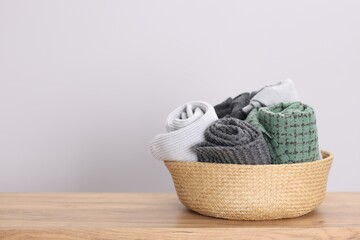 Wool scarves in wicker basket on wooden table indoors, space for text