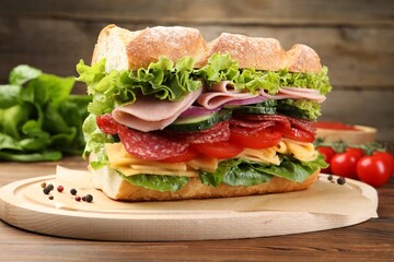 Tasty baguette sandwich with ham and vegetables on wooden table, closeup